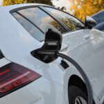 Ein weißes Elektroauto ist über ein eingestecktes Ladekabel an einer Ladestation angeschlossen.