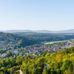 Panorama-Aussicht auf Bad Kissingen, umgeben von dicht bewaldeten Hügeln unter klarem, blauem Himmel.