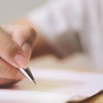 Eine Hand hält einen Kugelschreiber und setzt eine Unterschrift auf ein Dokument.
