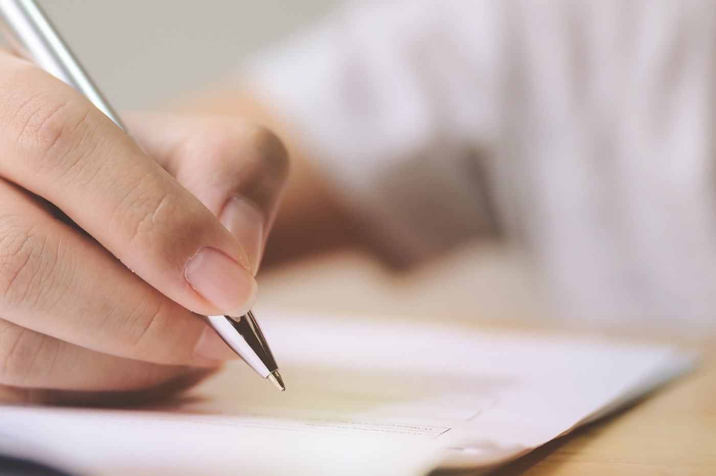 Eine Hand hält einen Kugelschreiber und setzt eine Unterschrift auf ein Dokument.