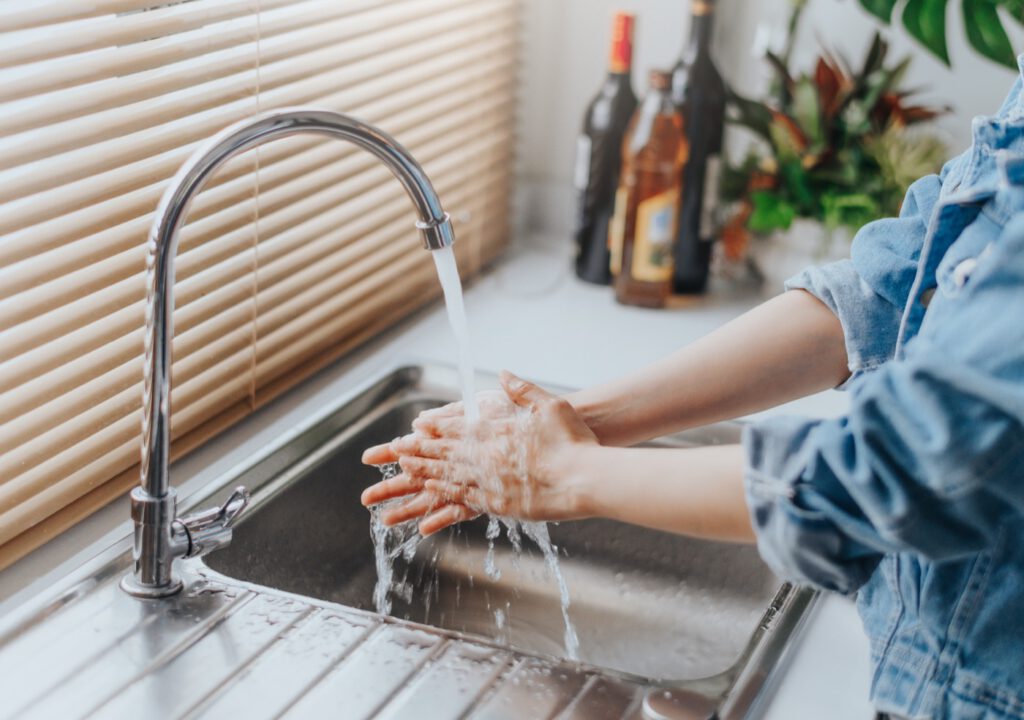 Eine Person wäscht sich die Hände unter fließendem Wasser an einer Küchenspüle.