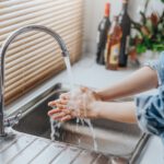 Eine Person wäscht sich die Hände unter fließendem Wasser an einer Küchenspüle.
