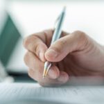 Eine Hand hält einen Kugelschreiber und setzt eine Unterschrift auf ein Dokument.