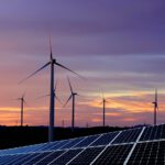 Mehrere Windkraftanlagen und eine große Photovoltaikanlage vor einem farbenprächtigen Abendhimmel.