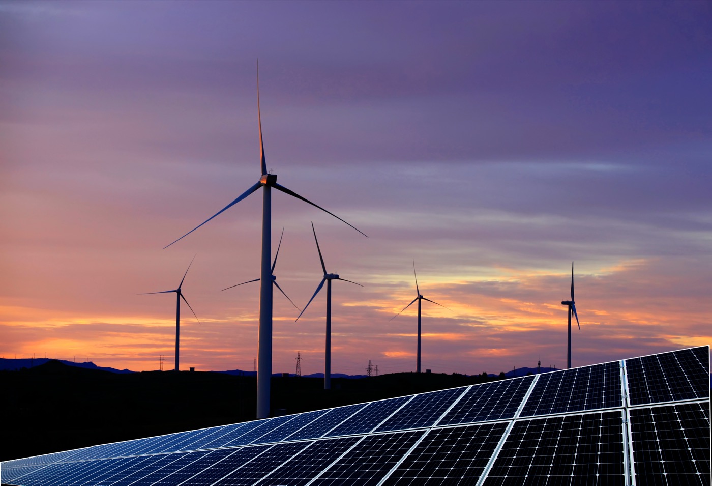 Mehrere Windkraftanlagen und eine große Photovoltaikanlage vor einem farbenprächtigen Abendhimmel.
