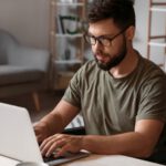 Ein junger Mann mit Brille und Bart arbeitet an einem Laptop.