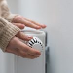 Frau umfasst mit der Hand den Temperaturregler eines Heizkörpers.