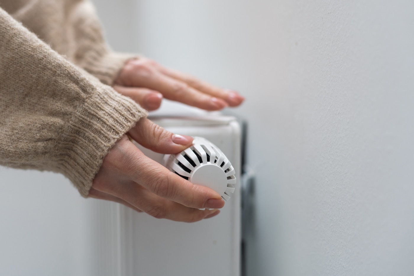 Frau umfasst mit der Hand den Temperaturregler eines Heizkörpers.