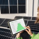 Eine Frau hält ein Tablet in der Hand und schaut sich ein Balkendiagramm an. Im Hintergrund sind verschiedene Photovoltaik-Paneele.