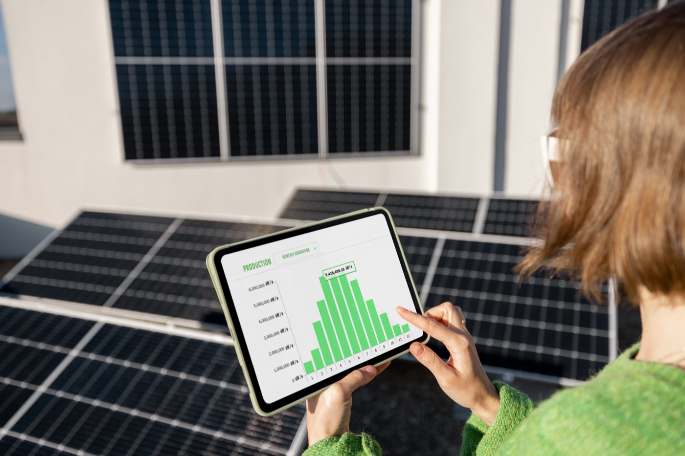 Eine Frau hält ein Tablet in der Hand und schaut sich ein Balkendiagramm an. Im Hintergrund sind verschiedene Photovoltaik-Paneele.