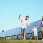 Eine große Photovoltaikanlage auf einer Wiese, davor eine junge Familie mit Vater, Mutter und Kleinkind.
