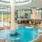 Die lichtdurchflutete Innen-Thermenlandschaft der KissSalis Therme mit einem großen Thermalbecken, Whirlpools und Liegebereichen unter einer großen Glaskuppel.