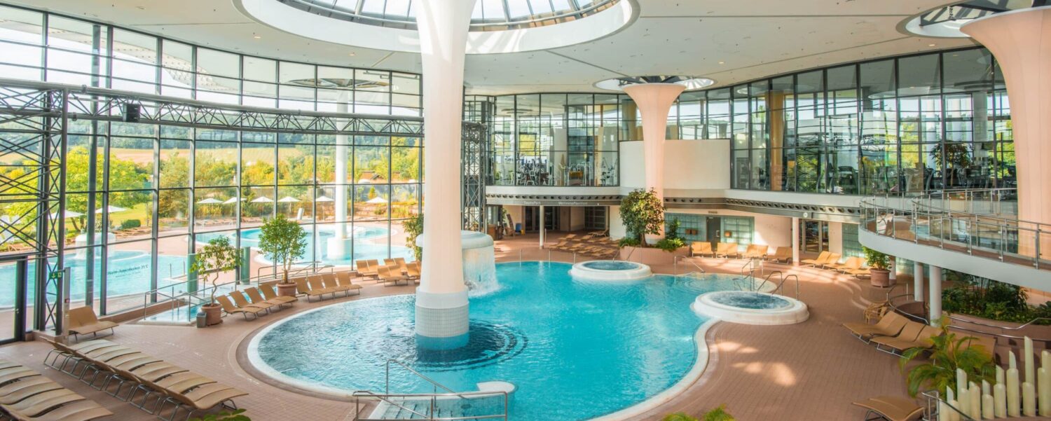 Die lichtdurchflutete Innen-Thermenlandschaft der KissSalis Therme mit einem großen Thermalbecken, Whirlpools und Liegebereichen unter einer großen Glaskuppel.