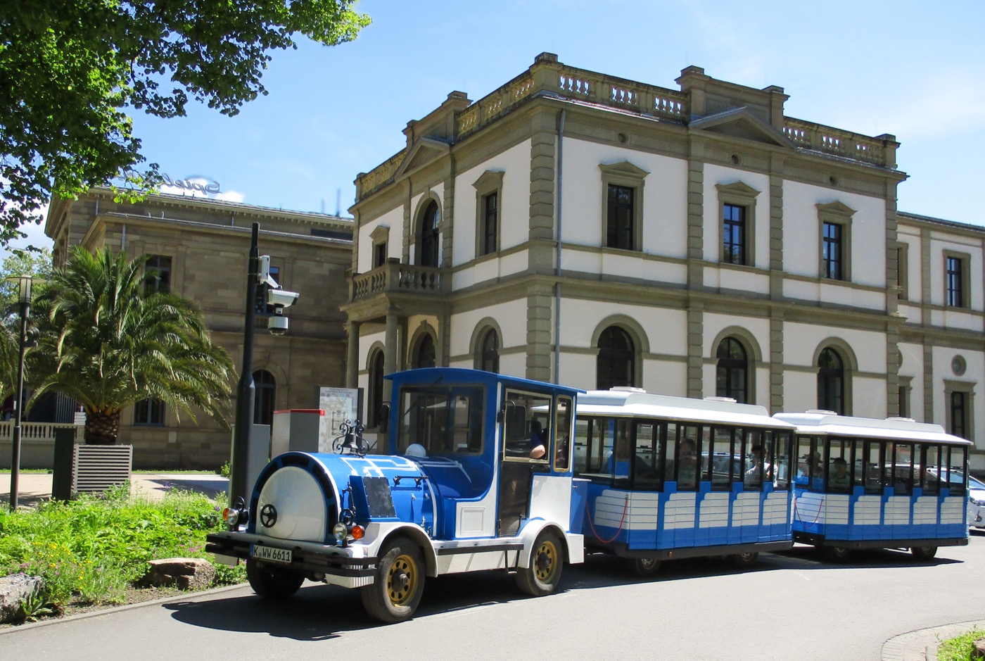 Das blau-weiße Kurbähnle steht vor einem historischen Gebäude.