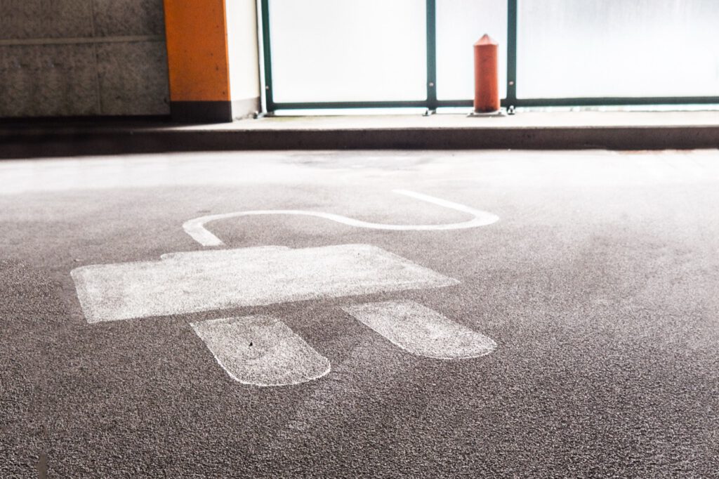 Ein markierter Parkplatz für Elektroautos mit einem großen, aufgemalten Steckersymbol auf dem Asphalt.