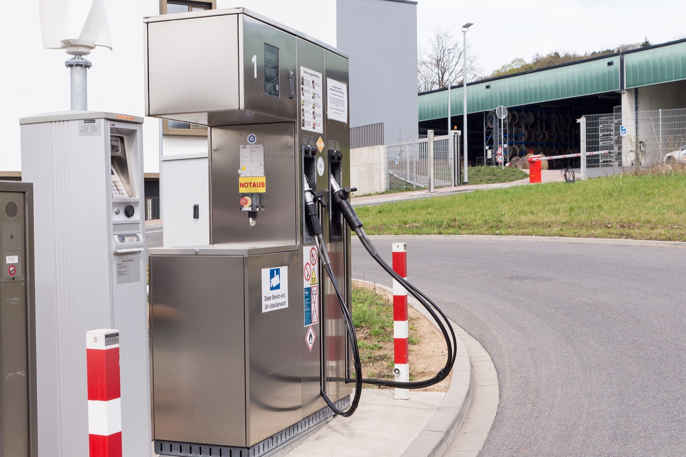 Eine moderne Erdgastankstelle (CNG/LNG) aus Edelstahl mit Zapfsäule, Bezahlterminal und Hinweisschildern an einer Zufahrtsstraße.